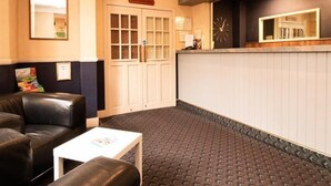 A lobby with a reception desk, a clock, a bulletin board, and a seating area with a coffee table.