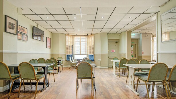 A conference room with multiple tables and chairs, a tiled ceiling, and framed artwork on the walls.