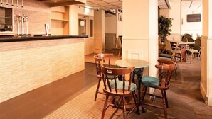 A hotel lobby with a reception desk, wooden chairs, a round table, and a potted plant.