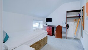 A bedroom with a bed, a desk, a chair, a wardrobe, and a television.