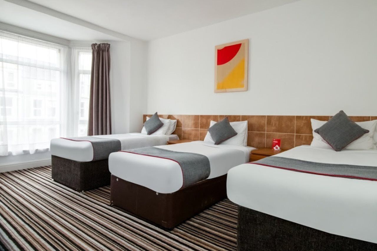 A hotel room with two beds, a large window with curtains, and a striped carpet.