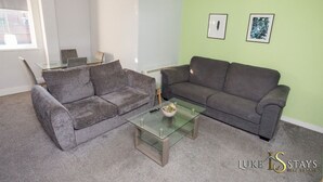A living room with two grey sofas, a glass coffee table, and a small plant. There is a window with blinds and two framed pictures on the wall. - 6 X APARTMENTS IN 1 BLOCK JUST OUTSIDE THE CITY ⭐MINUTES WALK FROM SHOPS⭐ APT#4 (Newcastle Upon Tyne)