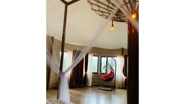A room with a bed, a hanging chair, and a large window. - Rustic Charm Wayanad - The Stump (Treetop Suite) (Appapara)