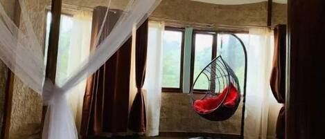 A room with a bed, a hanging chair, and a large window.