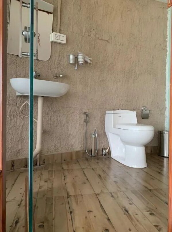 A bathroom with a wooden floor, a white sink, a toilet, and a shower.