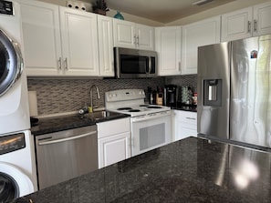 Features a well-lit kitchen with stainless steel appliances, white cabinetry, and a granite countertop.