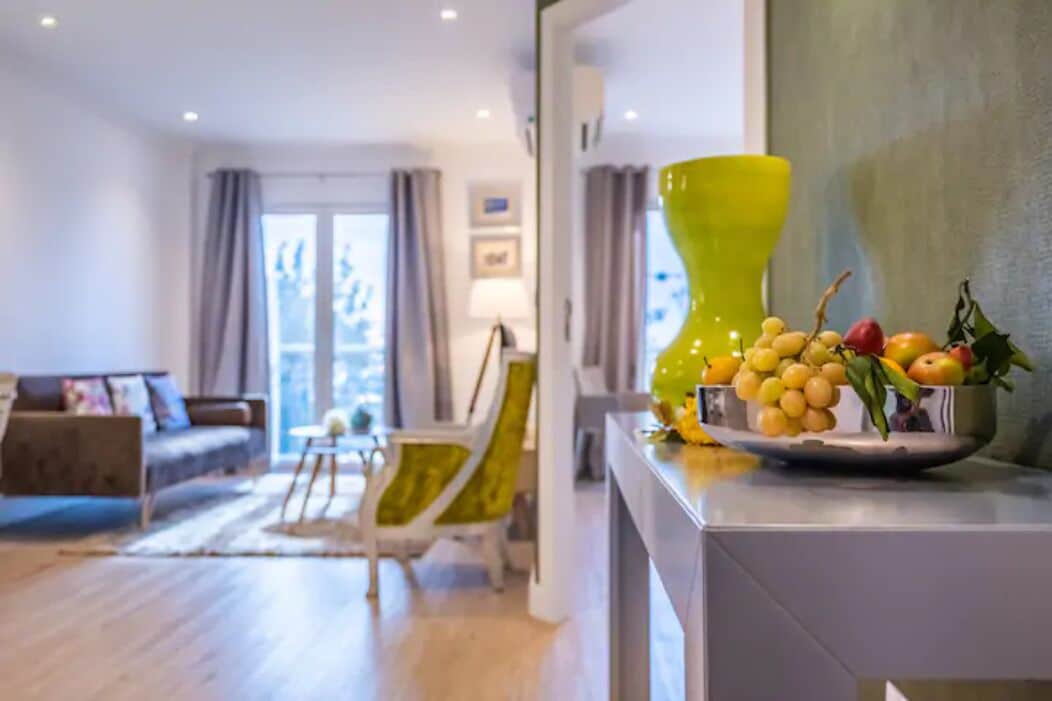 A modern living room with a sofa, a yellow chair, and a fruit bowl on a counter.