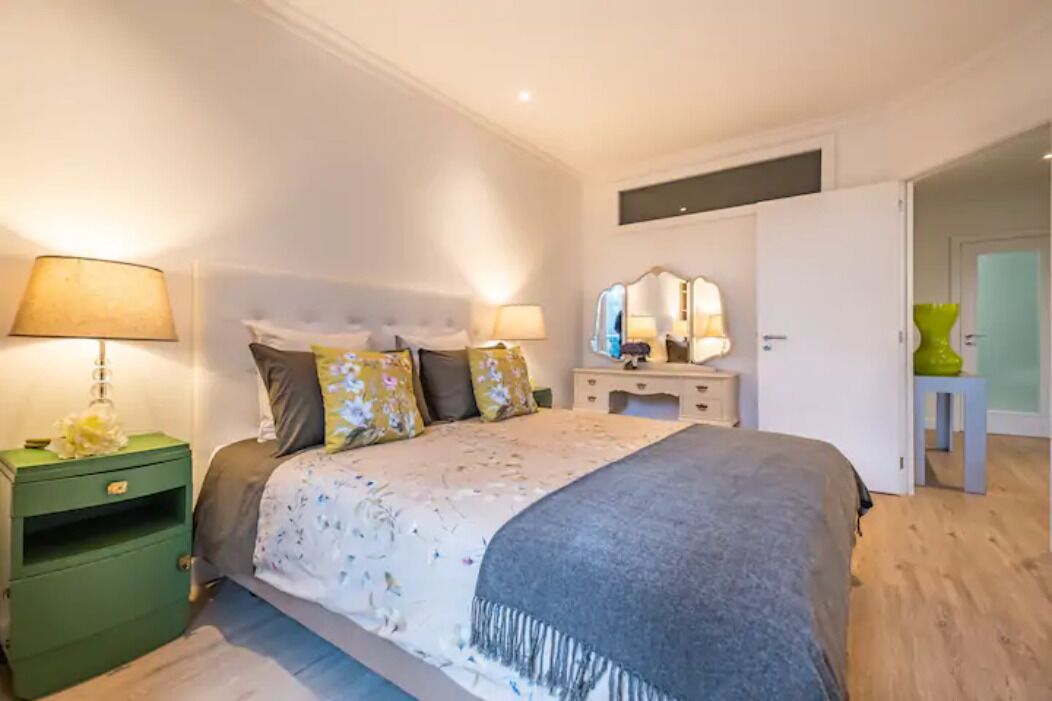 A bedroom with a bed, two bedside tables, a mirror, and a green nightstand.