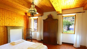 Una habitación con una cama, un armario de madera, una silla y un ventanal con cortinas.