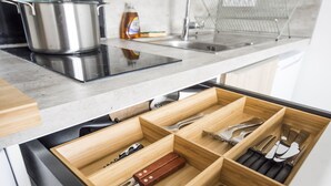 Uma cozinha com uma panela de aço inoxidável no fogão, uma pia e um organizador de gavetas de madeira com utensílios.