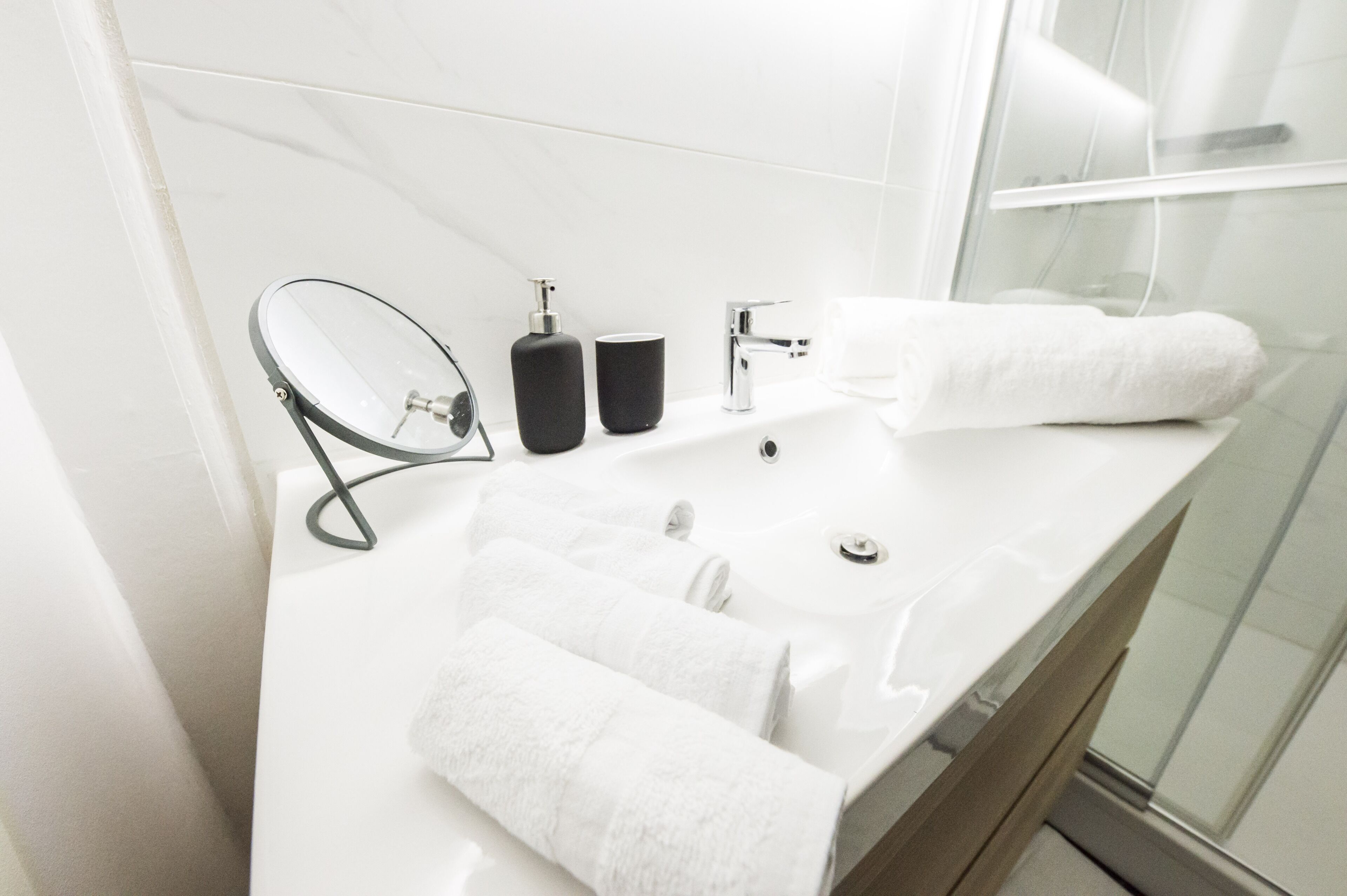 A modern bathroom with a white sink, two black soap dispensers, a white towel, and a glass shower enclosure.
