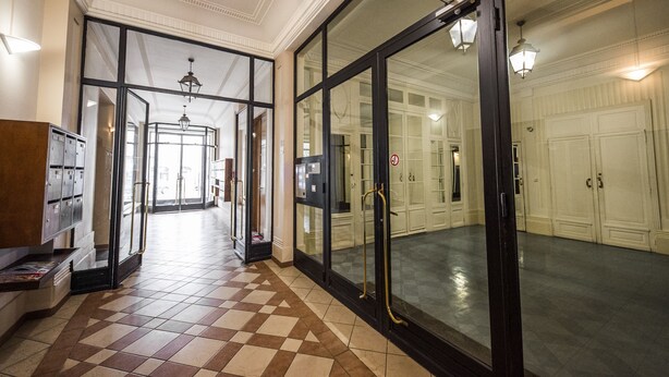 Um saguão de hotel com piso xadrez, um balcão de recepção e vista para um quarto com uma grande janela e uma porta.