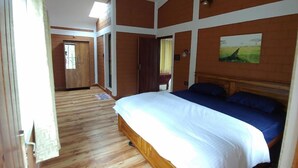 A bedroom with a large bed, wooden flooring, and a painting on the wall.