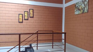 A staircase with metal railings leading to an upper floor, a brick wall with three framed artworks, and a window with a view of greenery.