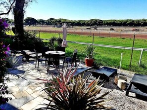 Un patio exterior con mobiliario, una parrilla y vistas a una pista de carreras.