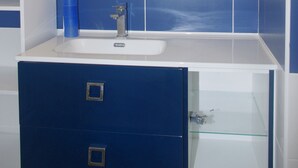 Une salle de bain avec un lavabo blanc, des carreaux bleus, un miroir et un meuble bleu avec des tiroirs.