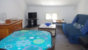 Un salon avec un canapé, un téléviseur, une table sur laquelle se trouve un bol bleu, et une nappe à motifs.