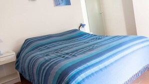 Une chambre à coucher comprenant un lit, une table de chevet, une lampe fixée au mur et une porte.
