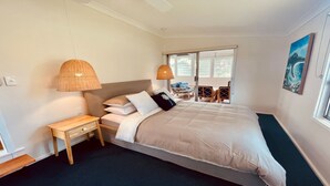 Quarto com cama grande, duas luminárias de cabeceira, mesa de apoio e vista para o exterior pela janela.