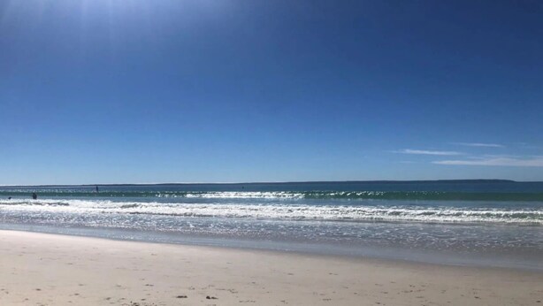 Uma praia com céu limpo e ondas calmas.