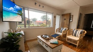 A living room with a television, wicker chairs, a coffee table, and a view of a beach through the window.