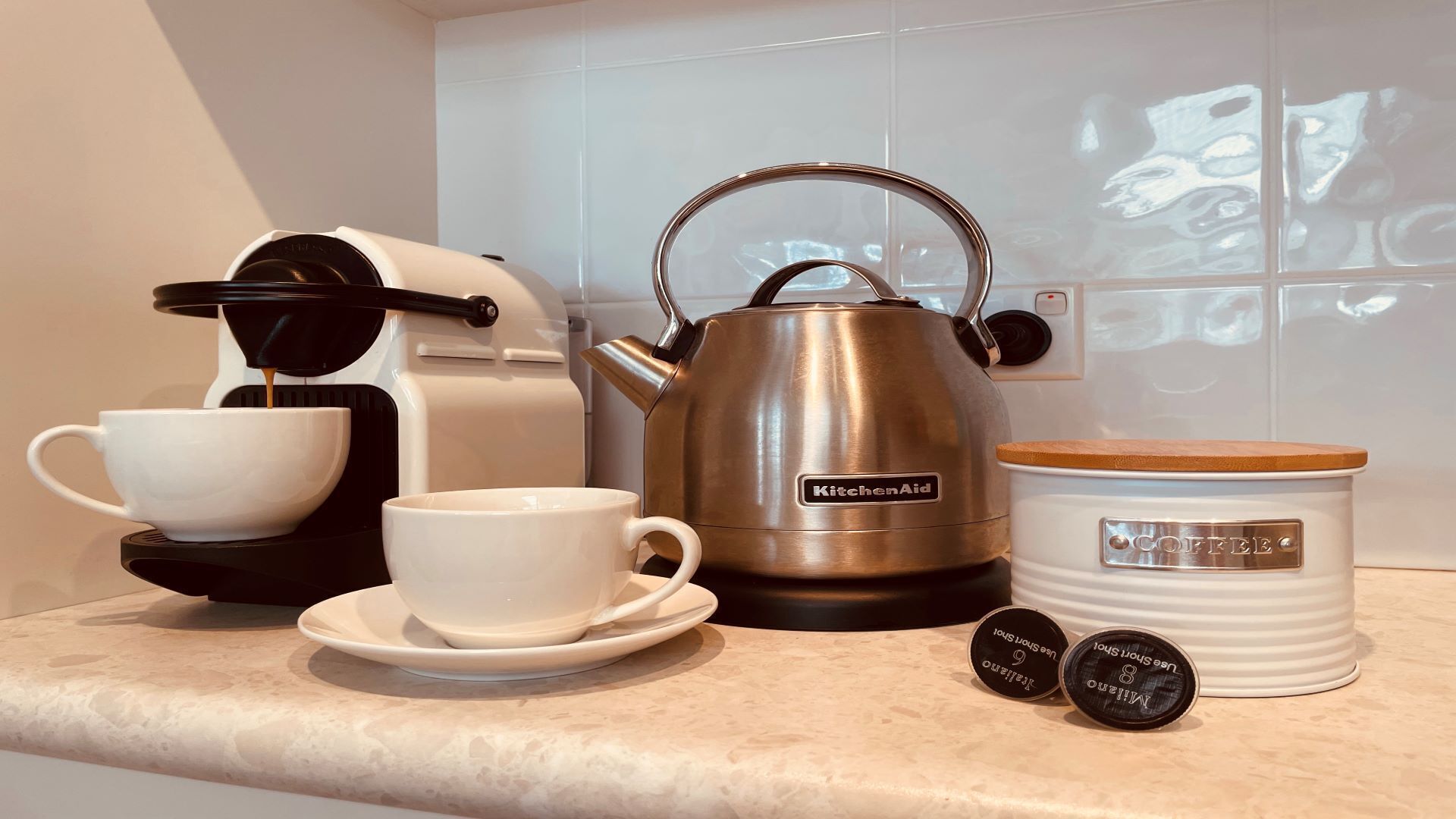 Een koffiehoek met een koffiezetapparaat, waterkoker, bekers en een koffievoorraadcontainer.