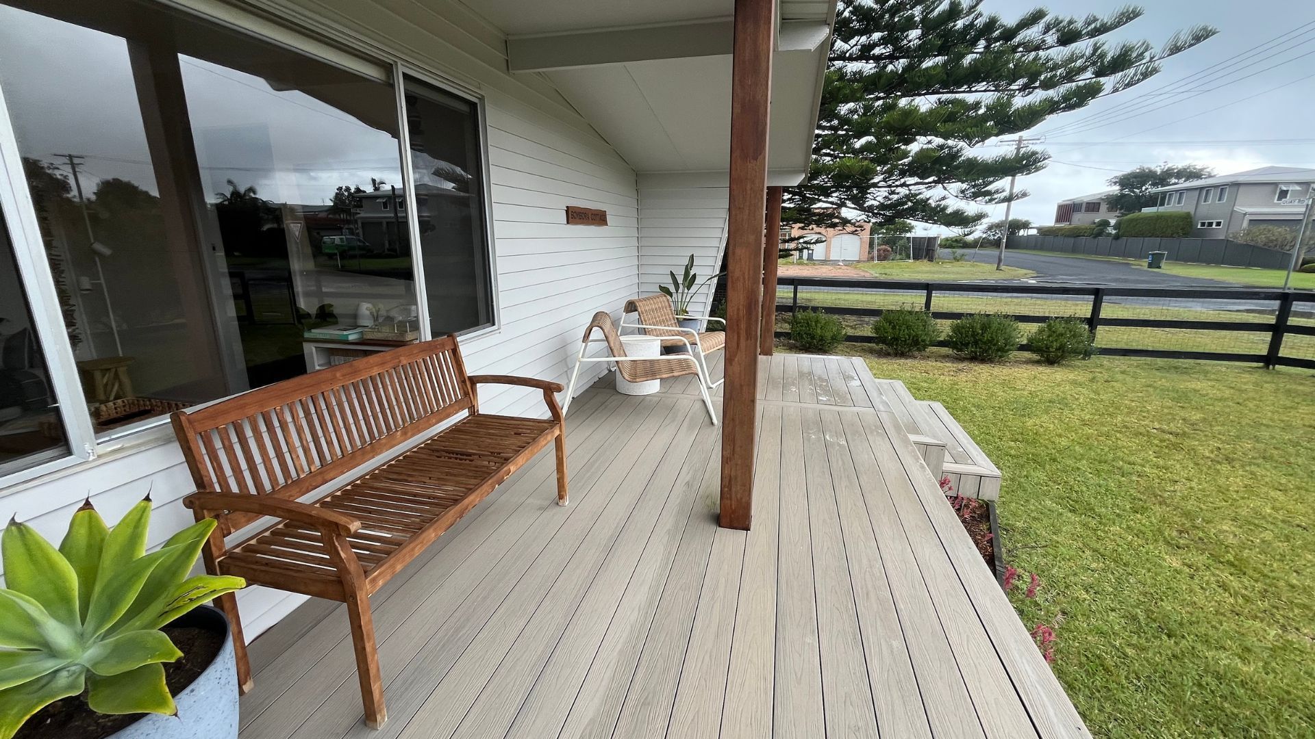 Une terrasse en bois avec un banc et des chaises, un pot de fleurs et une vue sur la rue.
