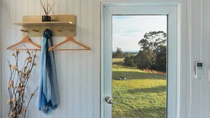 A door with a view of a grassy landscape, a wooden shelf with a candle, and a blue towel hanging on a wall.