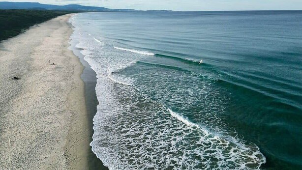 A beach with waves, a sandy shore, and distant mountains.