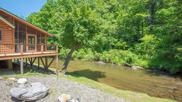 Een houten vakantiehuisje met een terras, met uitzicht op een rivier, omringd door weelderige begroeiing.