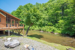 Une cabane en bois dotée d’une terrasse donnant sur une rivière, le tout entouré d’une végétation luxuriante.