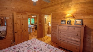 Een houten blokhut inrichting met een bed, een dressoir en een plafondventilator.