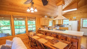 Een gezellige keuken in chaletstijl met houten kasten, een centraal eiland en een eethoek met een grote tafel en stoelen.