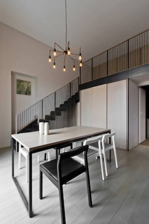 A modern dining area with a minimalist table and chairs, a staircase, and a unique pendant light fixture. - Luxury 1-bed Apartment in Vilnius Oldtown (Vilnius)