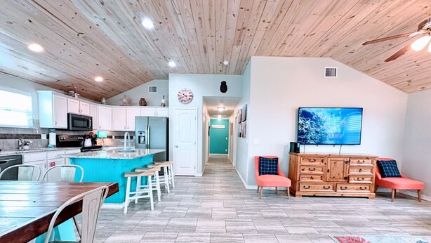 Una cocina moderna con armarios blancos, una isla central y un comedor con mesa y sillas de madera.