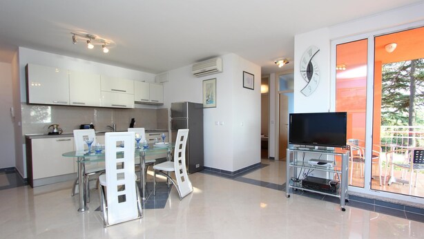 A modern kitchen with white cabinets, a dining area with a glass table, and a TV on a stand. - Apartment Nautica (Novigrad)