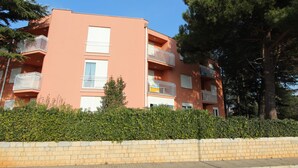 A multi-story residential building with balconies, a brick wall in the foreground, and trees in the background. - Apartment Nautica (Novigrad)