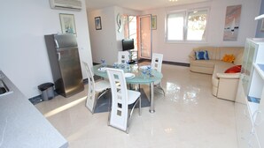 A modern kitchen with a refrigerator, dining table, and chairs. There is a sofa and a TV in the living area. - Apartment Nautica (Novigrad)