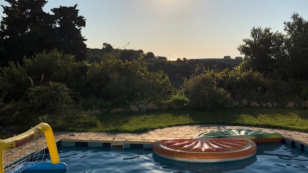 Zwembad met een jacuzzi en opblaasringen, omgeven door groen en een heldere lucht.