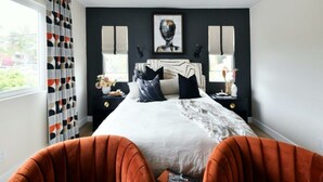 Une chambre à coucher avec un lit, deux tables de chevet, une fenêtre avec des rideaux et un tableau au mur.