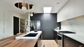 Une cuisine moderne avec un îlot central en bois, des meubles de rangement aux couleurs sombres et un dosseret en marbre.
