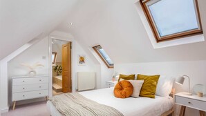 A bedroom with a sloped ceiling, a skylight, a bed with pillows, a bedside table with a lamp, and a dresser. - Sunset View - Donnini Apartments (Ayr)