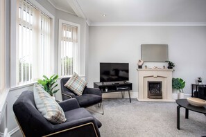 A living room with a fireplace, a television, and two sofas with cushions. - Sunset View - Donnini Apartments (Ayr)
