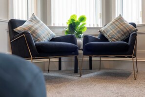 A room with two dark blue armchairs with gold legs, each with a plaid pillow, positioned on a carpeted floor. - Sunset View - Donnini Apartments (Ayr)