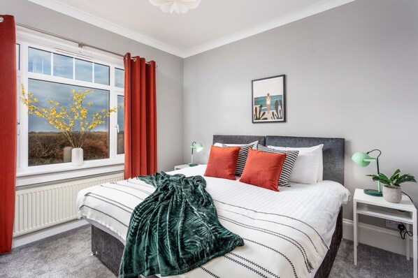 A bedroom with a bed, a nightstand, a window with curtains, a picture on the wall, and a plant on the nightstand. - Sunset View - Donnini Apartments (Ayr)