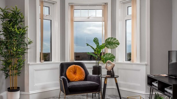 A modern living room with a black armchair, a round table, and a large window with a view. - Sunset View - Donnini Apartments (Ayr)