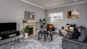 A modern living room with a fireplace, a flat-screen TV, a sofa, and a coffee table. - Sunset View - Donnini Apartments (Ayr)