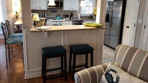 A modern kitchen with white cabinets, a stainless steel refrigerator, and a bar area with stools. - Wildlife Watching! Lagoon & Golf view, beach gear included. Peaceful & Private! (Hilton Head Island)
