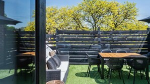 An outdoor patio with a wooden table and chairs, a wicker sofa, and a black fence. - Expansive open loft apartment in the middle of downtown. Great for groups. (Saratoga Springs)