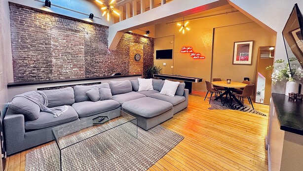 Un salon moderne avec un canapé d’angle, un plancher en bois, un mur en briques et une lucarne.